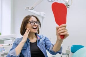 Woman patient looking in the mirror at the teeth, sitting in the dental chair. Healthcare, medical and dentistry concept.